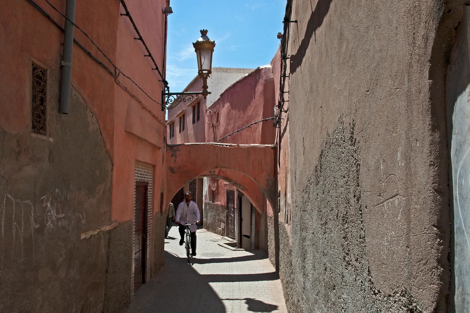 Callejuela de la medina de Marrakech con arco y muros rojizos, cerca de la mezquita Ben Youssef