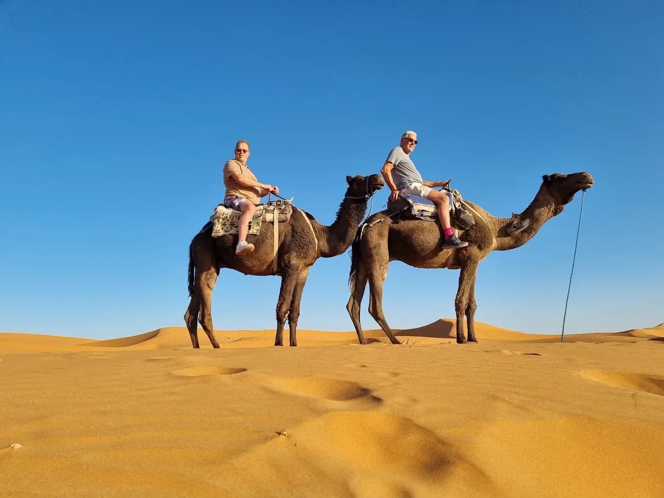 Dos viajeros en dromedario en las dunas