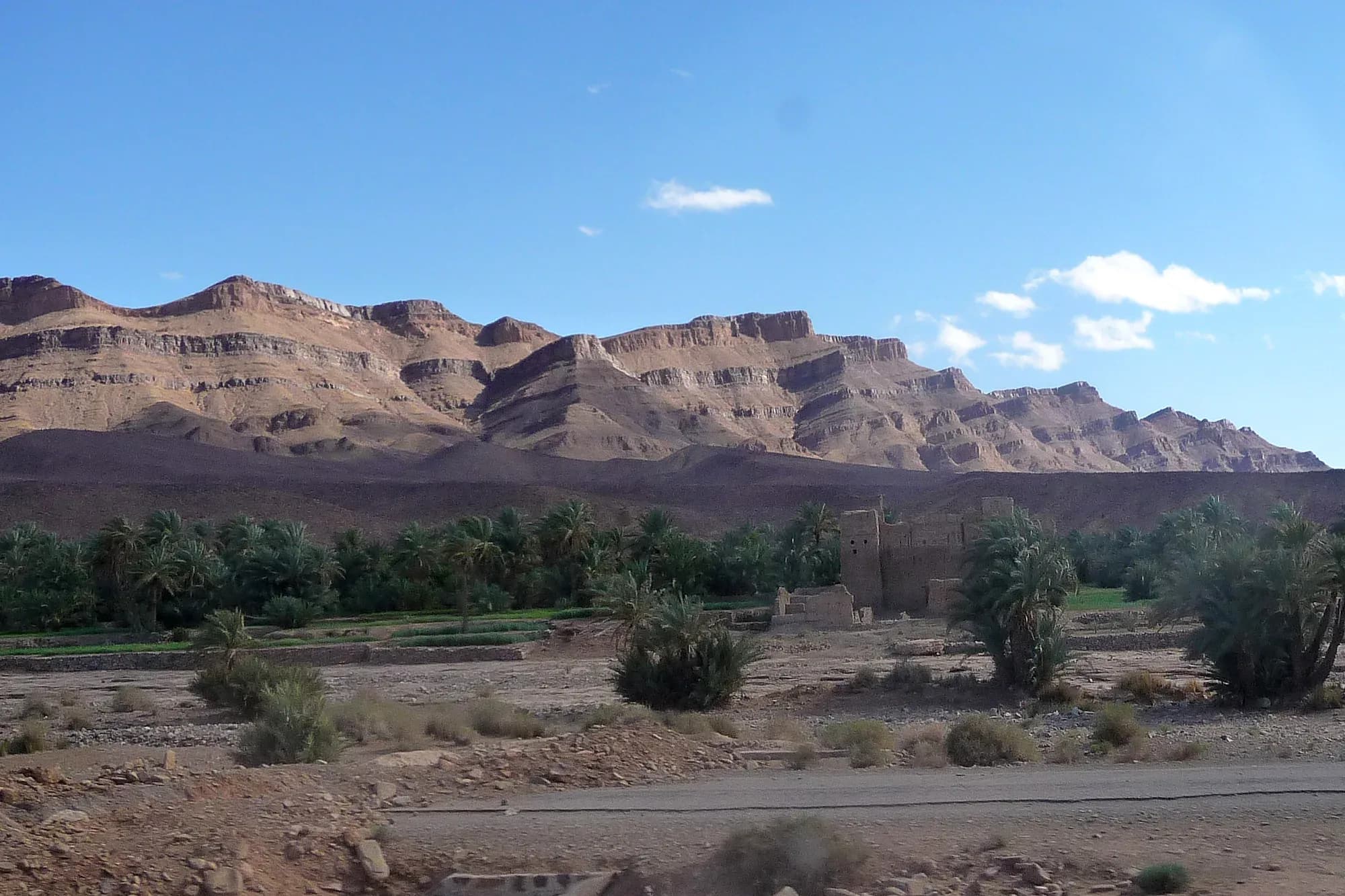 Carretera junto a un palmeral y mesetas rocosas cerca de Tazzarine