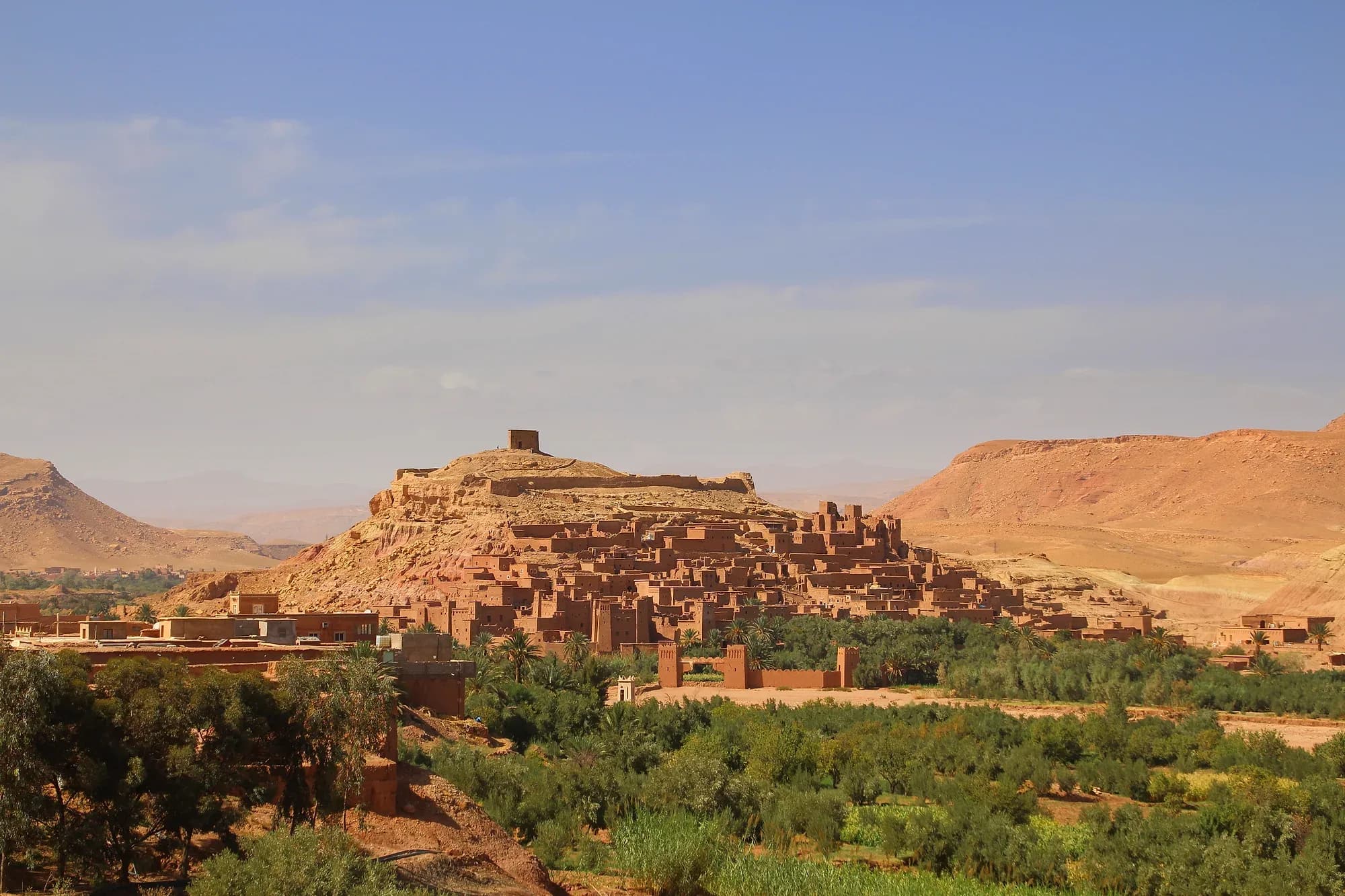 Vista panorámica del ksar de Aït Ben Haddou sobre su colina, con el palmeral y las montañas al fondo