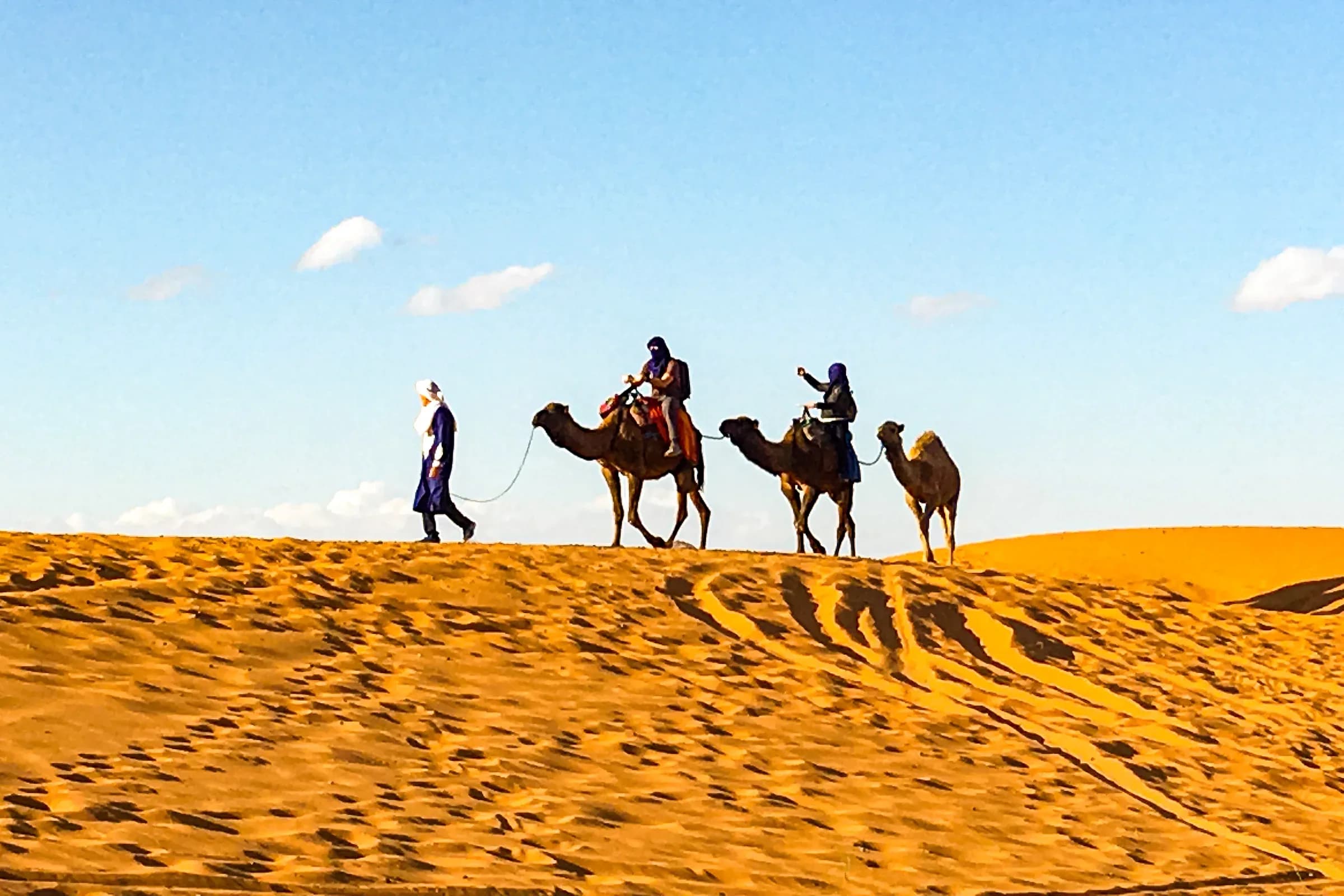 Caravana de dromedarios con viajeros sobre una duna de Erg Chebbi