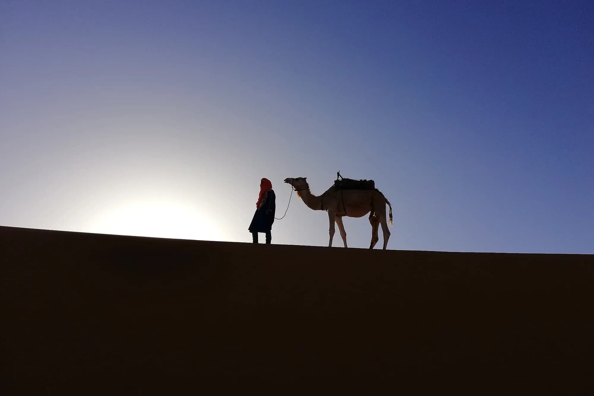 Silueta de un camellero y su dromedario en lo alto de una duna al anochecer, Merzouga