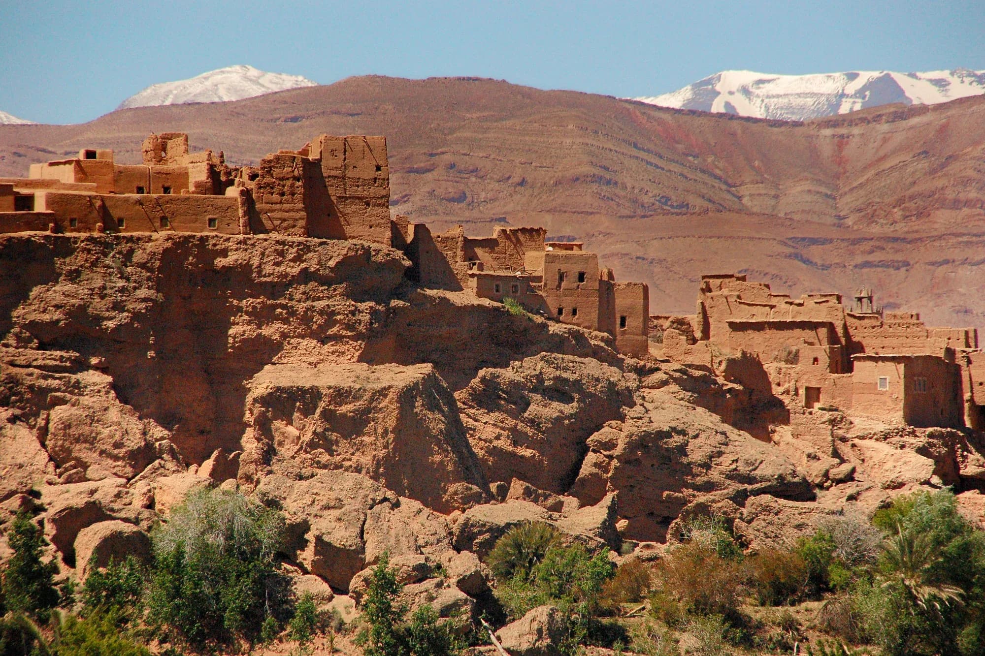 Kasbah de adobe sobre las rocas en la zona de Kelaat M'Gouna con el Alto Atlas nevado al fondo