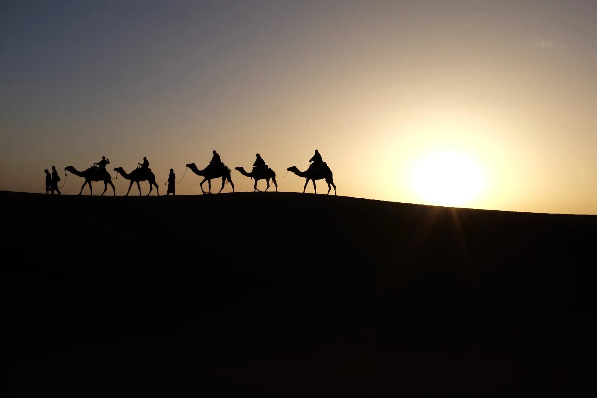 Siluetas de una caravana de dromedarios al atardecer sobre una duna de Merzouga