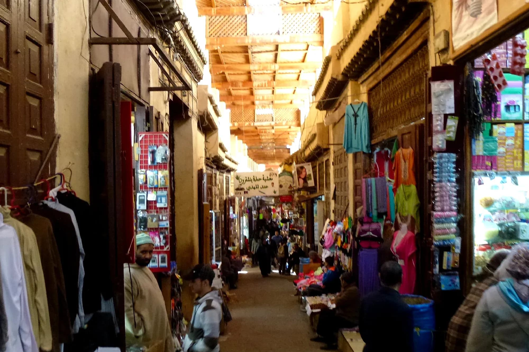Calle comercial cubierta de la medina de Fez el Bali con tiendas de ropa y paseantes
