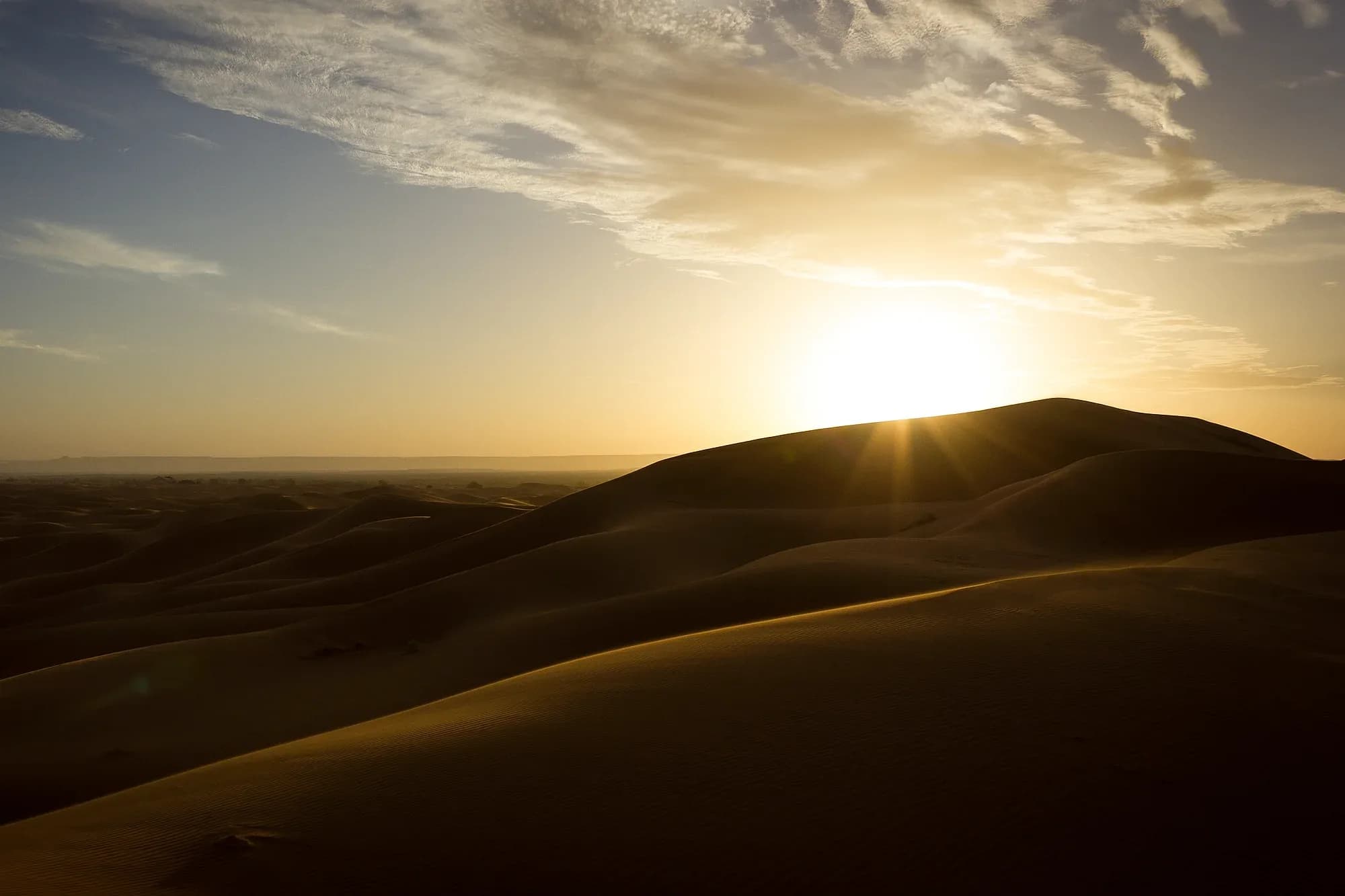 Rising sun over the Erg Chebbi dunes under a cloudy sky, near Merzouga